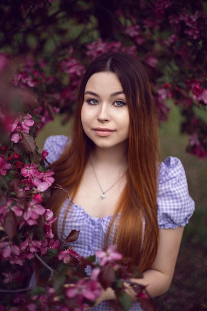 Retrato joven hermosa niña adolescente en un vestido morado se encuentra junto a un manzano rosa floreciente