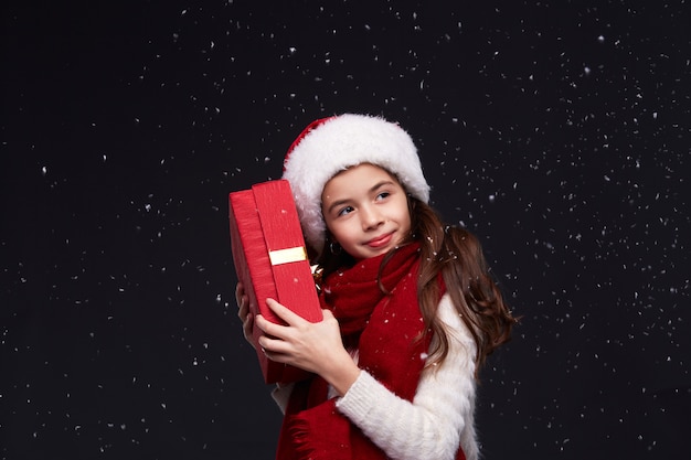 Retrato de joven hermosa niña sonriente con sombrero rojo de Santa sobre un fondo oscuro