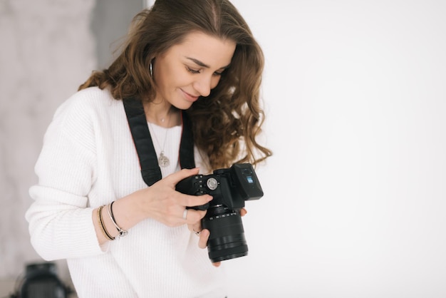 El retrato de una joven hermosa revisa las imágenes en la pantalla de la cámara en un estudio fotográfico ligero. Concepto de trabajo creativo en estudio fotográfico, trabajo entre bastidores.