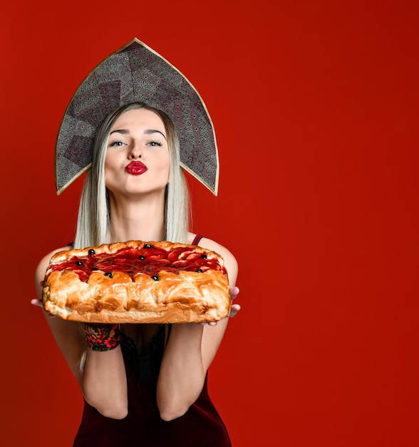 Retrato de una joven y hermosa rubia con pañuelo en la cabeza sosteniendo un delicioso pastel de cereza casero