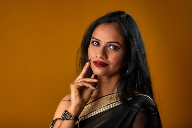 Retrato de una joven hermosa con sari negro tradicional posando sobre un fondo marrón