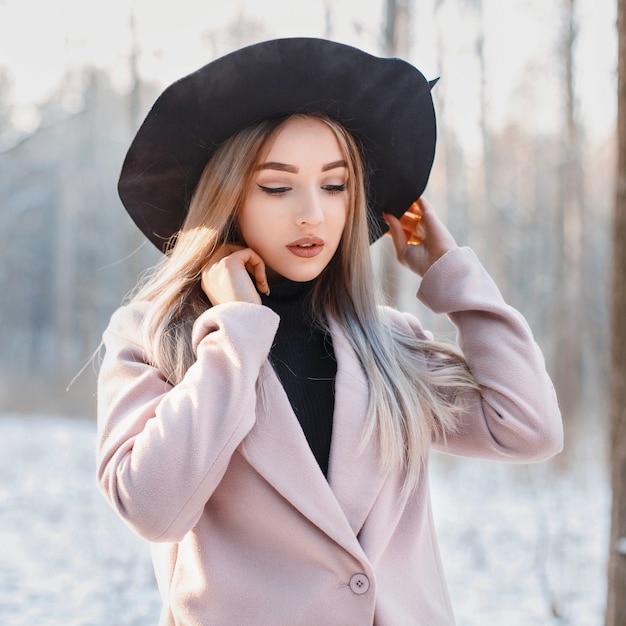 Retrato de una joven hermosa con un sombrero negro en un día de invierno al atardecer