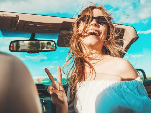 Retrato de joven hermosa y sonriente hipster en coche descapotable