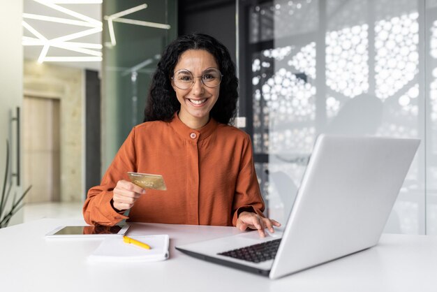 Foto retrato de una joven hispana que trabaja en la oficina usando una computadora portátil con una tarjeta de crédito y