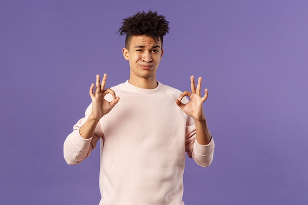 Foto el retrato del joven hispano escéptico califica algo de calidad normal, muestra un signo bien y hace una mueca de juicio, diciendo que no es malo, pero promedio