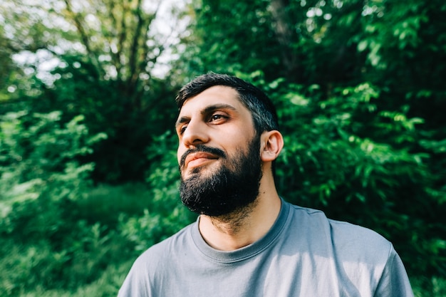 Retrato de joven hombre barbudo caucásico al aire libre con fondo de vegetación