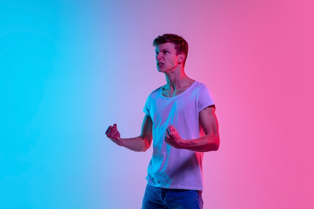 Retrato de joven hombre caucásico sobre fondo de estudio azul-rosa degradado en luz de neón