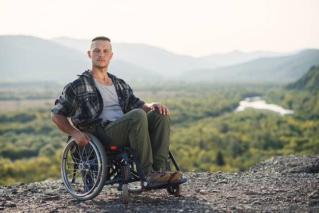 Retrato de joven hombre motivado de voluntad fuerte en una silla de ruedas disfrutando de la belleza de la naturaleza en el