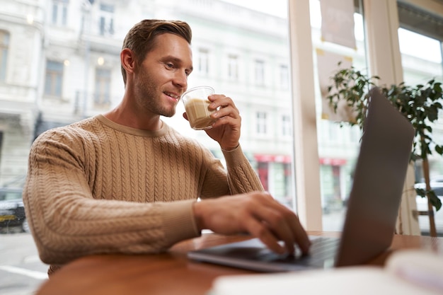 Retrato de un joven hombre de negocios en un café bebiendo café y usando su portátil trabajando desde