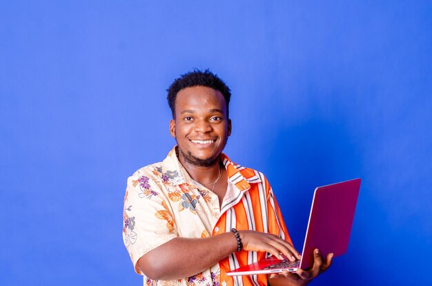 Retrato de un joven hombre de negocios moderno de pie sosteniendo una laptop y mirando a la cámara con una sonrisa feliz