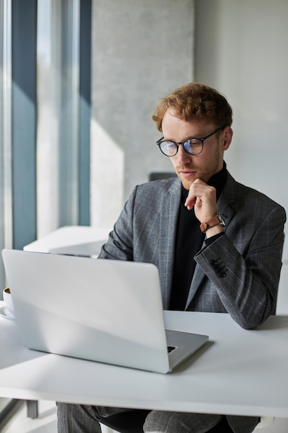 Retrato de un joven hombre de negocios que trabaja a distancia en una computadora portátil desde un interior de oficina moderno y ligero