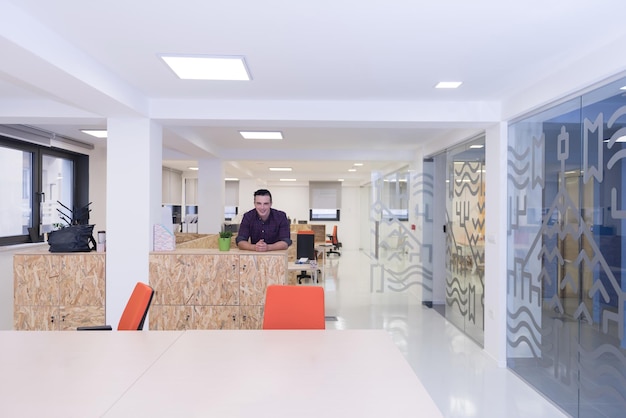 retrato de un joven hombre de negocios con ropa informal sentado en la mesa en un nuevo espacio de oficina y trabajando en una tableta