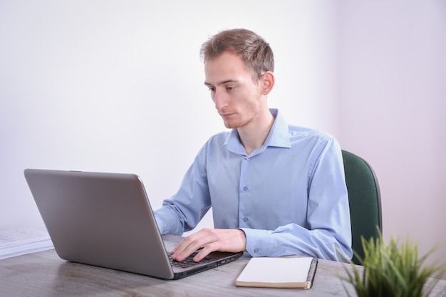 Retrato de joven hombre de negocios sentado en su escritorio, la tecnología portátil de escritorio en la oficina. Marketing en Internet, finanzas, concepto de negocio