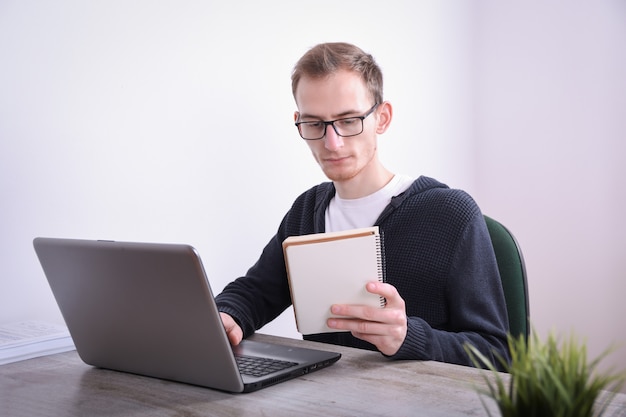 Retrato de joven hombre de negocios sentado en su escritorio con tecnología portátil en la oficina. Marketing en Internet, finanzas, concepto de negocio