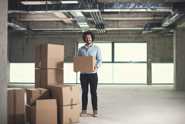 retrato de un joven hombre de negocios en el sitio de construcción revisando documentos y flujo de trabajo de negocios con cajas de cartón a su alrededor en una nueva oficina de inicio