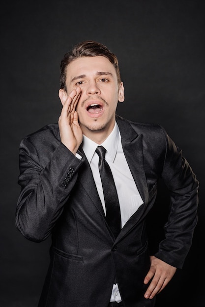 Retrato joven hombre de negocios en traje negro gritando con las manos abiertas emociones expresiones faciales sentimientos lenguaje corporal signos imagen sobre un fondo de estudio negro