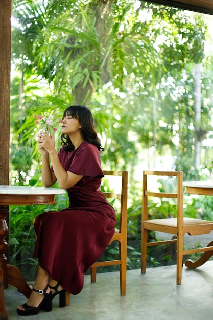 Retrato de una joven india en una cafetería con un ambiente relajado, una mujer asiática de piel bronceada vestida de púrpura siente una sonrisa feliz en la naturaleza tranquila y café helado con el sol de la mañana a través de una cortina de encaje