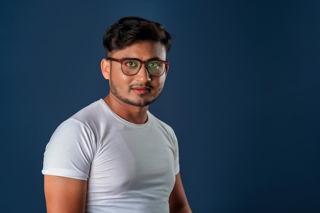 Retrato de un joven indio feliz con anteojos posando sobre un fondo azul