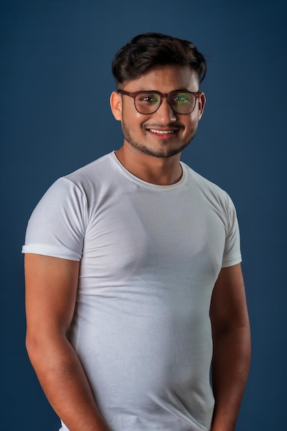 Retrato de un joven indio feliz con anteojos posando sobre un fondo azul