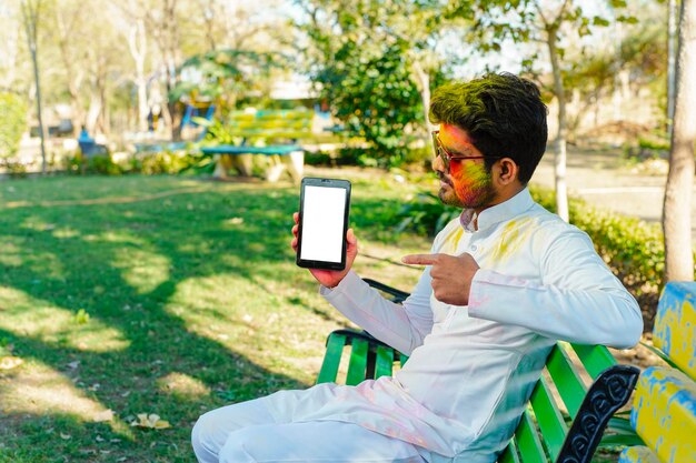 Retrato de un joven indio feliz en el festival de color holi usando un teléfono móvil