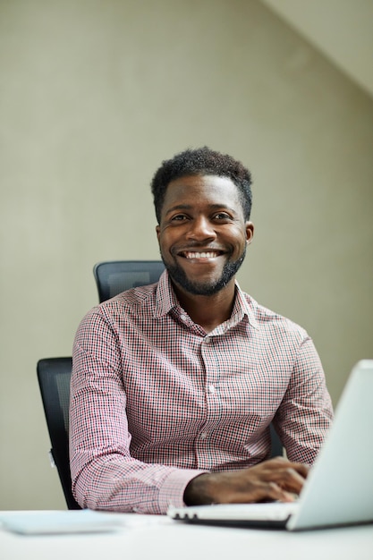 Retrato de un joven ingeniero afroamericano barbudo positivo sentado frente a una computadora portátil en un moderno o