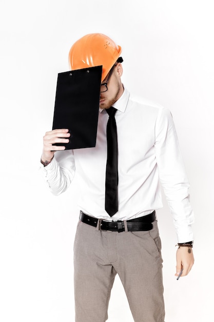 Retrato de joven ingeniero de la construcción en casco naranja con una carpeta sobre un fondo blanco.