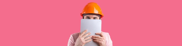Retrato de un joven ingeniero de construcción que usa un sombrero duro naranja en una chaqueta rosa de pie sobre un fondo rojo de estudio Un hombre con una tableta en las manos