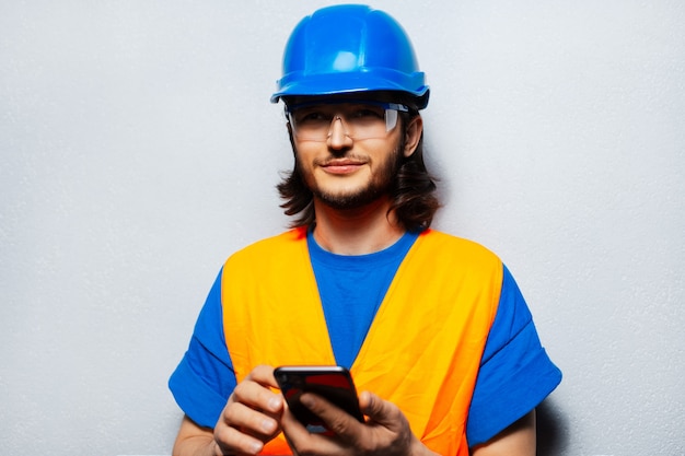 Retrato de joven ingeniero trabajador de la construcción reflexivo vistiendo equipo de seguridad con smartphone