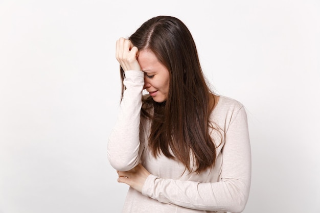 Retrato de una joven insatisfecha llorando molesta con ropa ligera poniendo la mano en la cabeza baja aislada en el fondo blanco del estudio. Emociones sinceras de la gente, concepto de estilo de vida. Simulacros de espacio de copia.