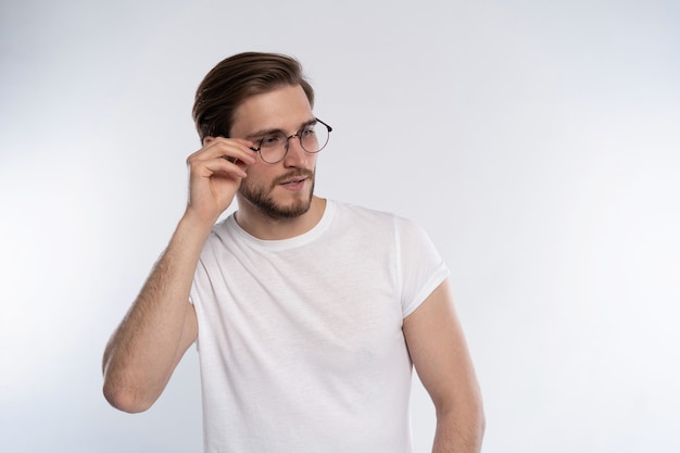 Retrato de un joven inteligente con gafas de pie contra el fondo blanco.