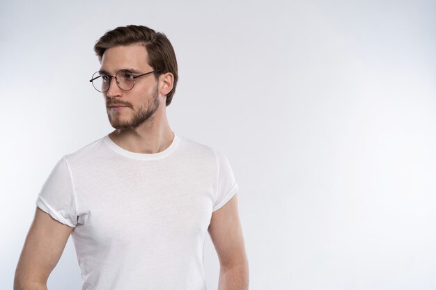 Retrato de un joven inteligente con gafas de pie contra el fondo blanco.