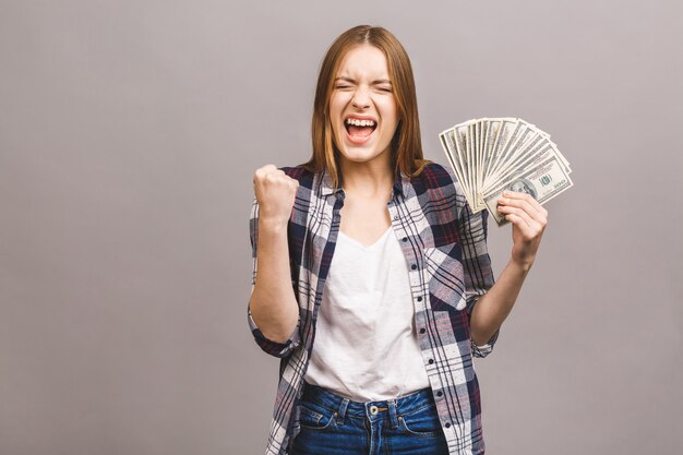 Retrato de una joven juguetona con el pelo largo que sostiene un montón de billetes de dinero y mirando a la cámara