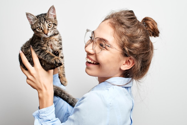 Retrato de una joven kazaja asiática alegremente sonriente jugando con un gatito en un estudio blanco