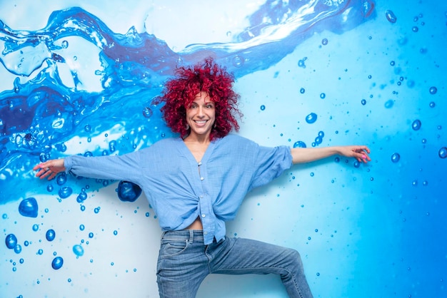 Retrato de una joven latina sonriente con el pelo afro rojo posando sobre un fondo azul con gotas azules