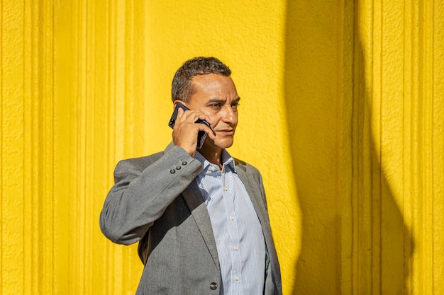 Retrato de un joven latino hablando por teléfono móvil aislado de fondo amarillo