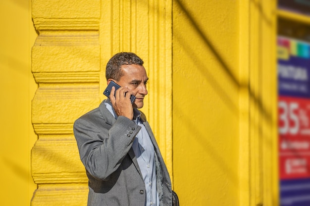 Retrato de un joven latino hablando por teléfono móvil sobre una pared amarilla con espacio para copiar