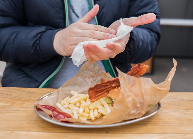 Retrato de joven limpiarse las manos con una toallita húmeda antes de comer hamburguesa