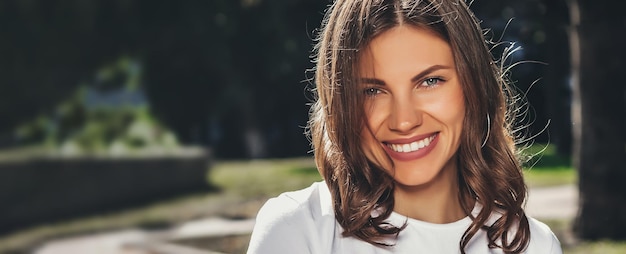 Retrato de una joven linda en una camiseta blanca con una sonrisa en el parque Chica atractiva sonriendo en el parque y mirando a la cámara