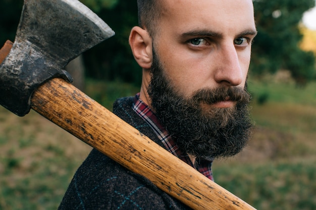 Retrato de joven logger barbudo hipster con hacha en bosque