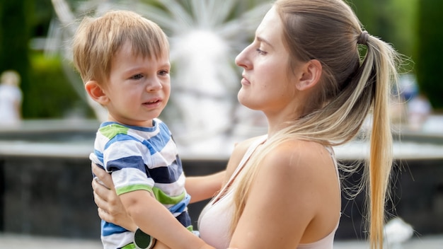 Retrato de joven madre acariciando y calmando a su hijo pequeño llorando en el parque