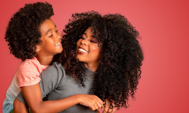 Retrato de joven madre afroamericana con hijo pequeño. Fondo rojo. Familia brasileña.