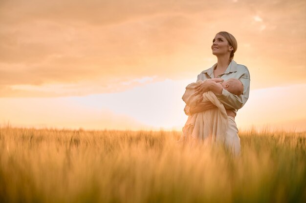 Un retrato de una joven madre con un bebé en sus brazos al atardecer en el concepto de familia feliz de campo