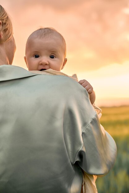 Un retrato de una joven madre con un bebé en sus brazos al atardecer en el concepto de familia feliz de campo