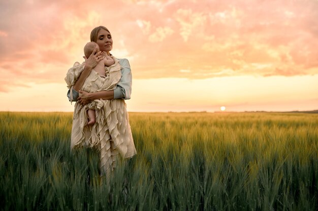 Un retrato de una joven madre con un bebé en sus brazos al atardecer en el concepto de familia feliz de campo