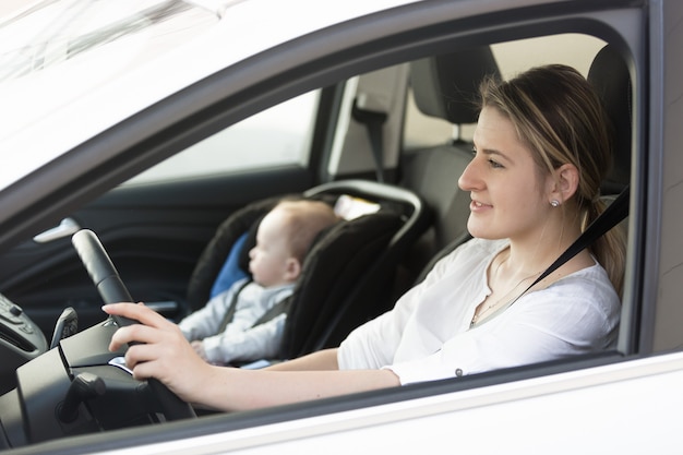 Retrato de joven madre en coche con su pequeño bebé en el asiento delantero