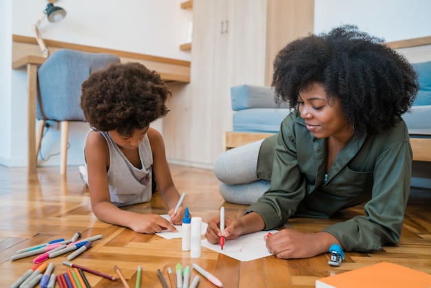 Retrato de joven madre e hijo afroamericanos dibujando con lápices de colores en un piso cálido en casa. Concepto de familia.