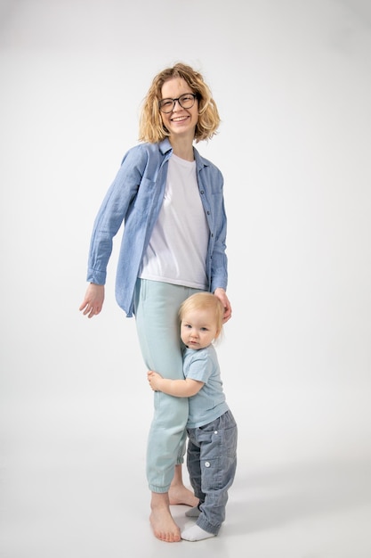 Retrato de una joven madre feliz vestida con pantalones deportivos color turquesa y una camisa vaquera abrazada por sm