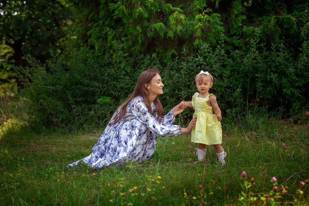 Retrato de joven madre joven con estilo feliz juega con su pequeña hija en el jardín verde