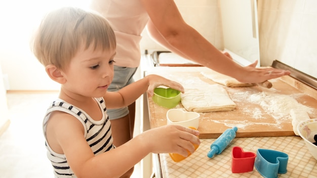 Retrato de joven madre sonriente enseñando a su niño de 3 años para hornear y hacer galletas en la cocina