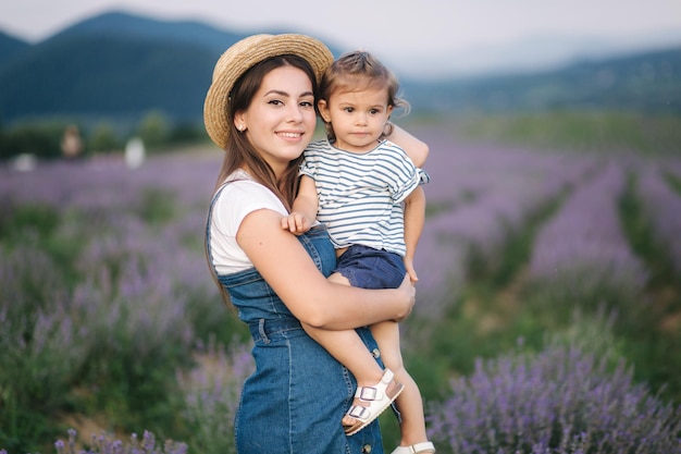 Retrato de joven madre con su adorable hija en el campo de lavanda de verano Estilo de mezclilla familiar Mujer con sombrero de paja